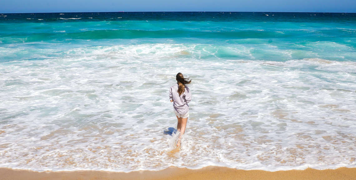 Frau steht mit wehendem Haar am Meer