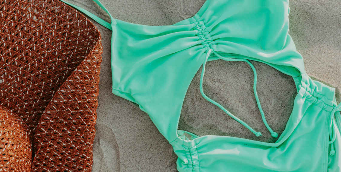 Bikini und Hut liegen auf Sand